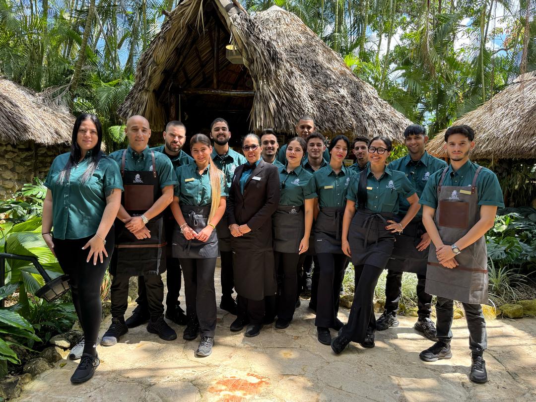 Equipo de Finca La Pinta frente al bohío, rodeado de palmeras.
